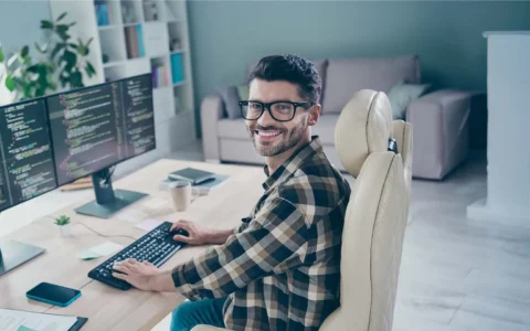Ingeniero en informática programando frente a múltiples monitores con código en oficina.