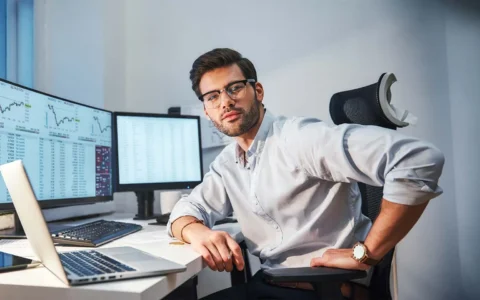 Técnico en análisis de datos trabajando en una oficina frente a múltiples monitores con gráficos y tablas estadísticas.