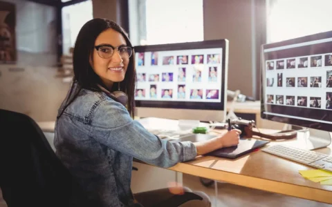 Técnica en diseño gráfico trabajando con tableta digitalizadora frente a dos monitores con múltiples imágenes en pantalla
