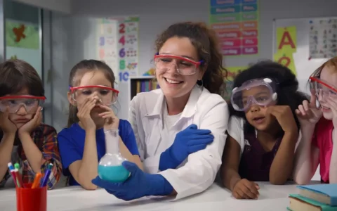 Técnica en educación parvularia realizando experimento con niños usando gafas de seguridad en sala de clases.