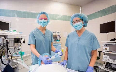 Equipo de anestesistas prepara paciente en pabellón, con mascarillas, gorros quirúrgicos y equipo médico especializado activo.