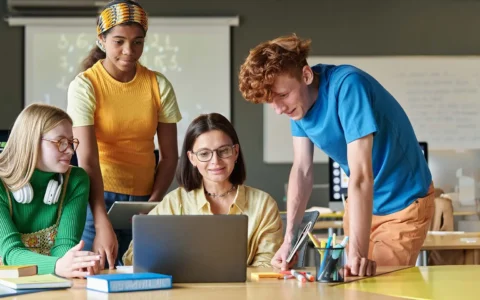 Técnica en trabajo social frente a computador colaborando con grupo de estudiantes.