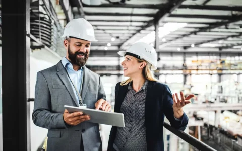 Ingenieros industriales con casco de seguridad revisando información en tablet dentro de planta de manufactura.