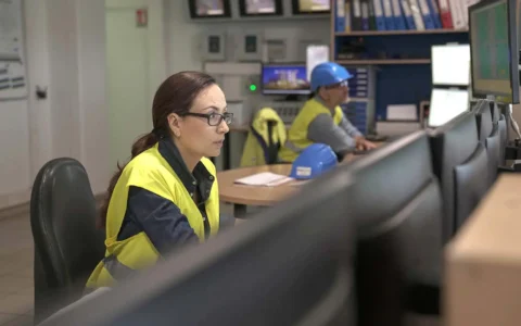 Técnicos en gestión de procesos mineros monitoreando sistemas desde sala de control con múltiples pantallas y equipos de seguridad.