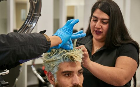 Estudiante de Técnico en Peluquería trabajando en la tintura de cabello de un cliente en un taller de una sede AIEP.