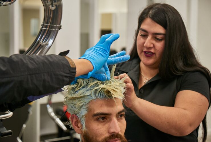Estudiante de Técnico en Peluquería trabajando en la tintura de cabello de un cliente en un taller de una sede AIEP.