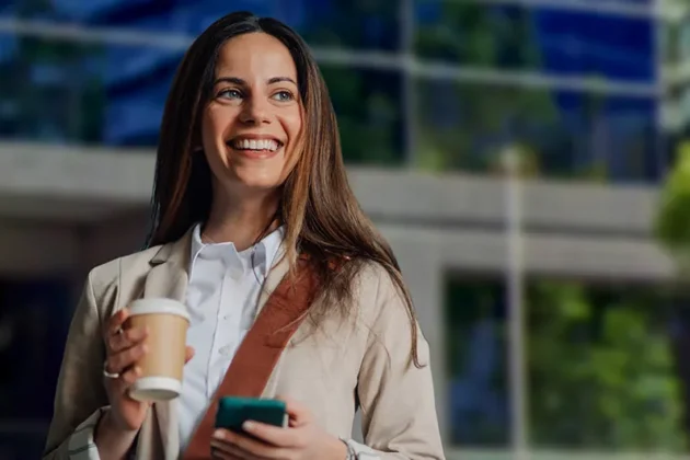 Alumna de AIEP con café y celular en mano frente al campus