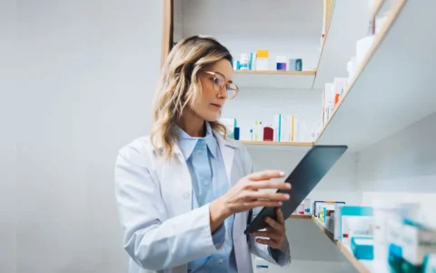 Técnico en Farmacia revisando medicamentos y registros digitales en farmacia